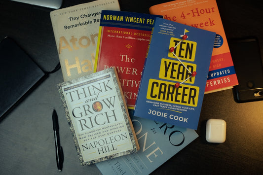 Top self-improvement books like Atomic Habits, Think and Grow Rich, and The 4-Hour Workweek on a desk.
